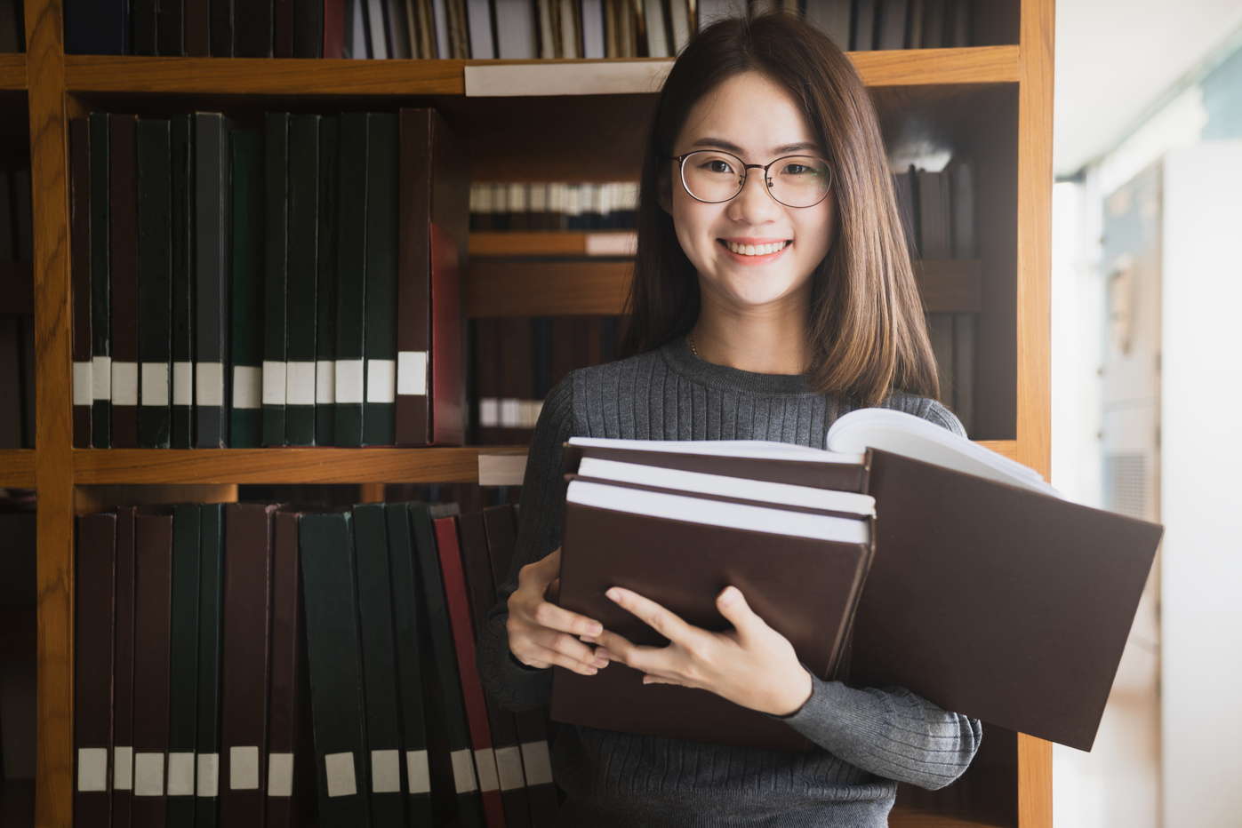 Education first, Beautiful female college student holding her books smiling happily standing in library, Education learning high school program smart teenager concept, Learning and education concept